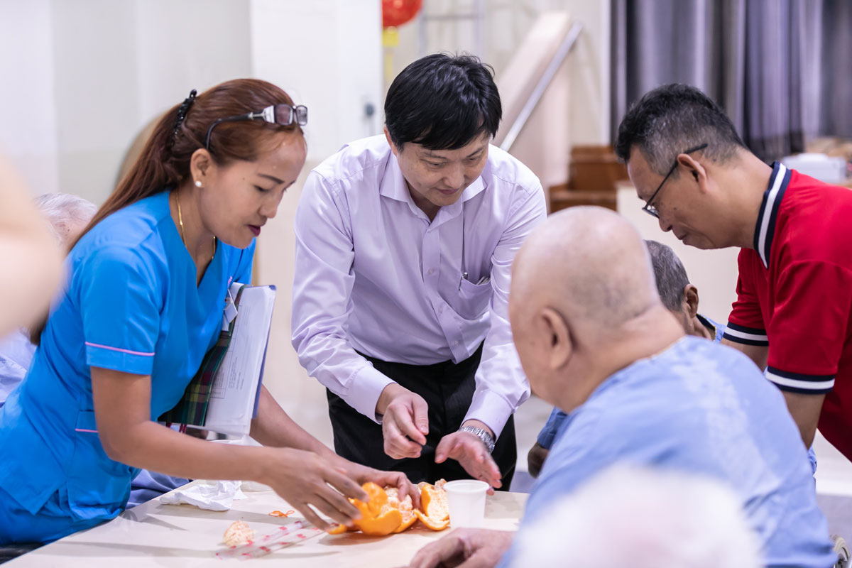Nurse and man peeling mandarin oranges for old folks